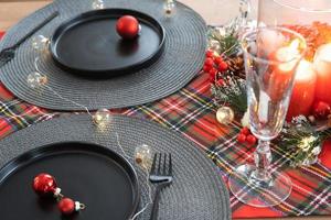 Festive table set in the living room for Christmas and New year in loft style. Christmas tree, black plates and forks, woven napkins, trendy tableware, cozy interior of the house photo