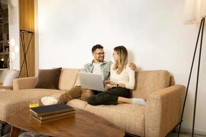 Young couple using laptop together while sitting on sofa at home photo