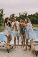 Young people standing by the swimming pool and eating watermellon in the house backyard photo