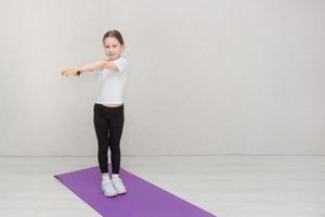 little girl goes in for sports at home, makes torso turns with a gymnastic stick photo