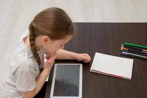 Grodno, Belarus - April 28, 2022 little girl with a pigtail at the table plays a game in a tablet, she thought about the next move photo