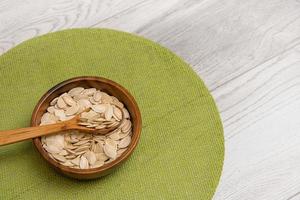 pumpkin seeds in a wooden plate with a wooden spoon on a green napkin, healthy products photo