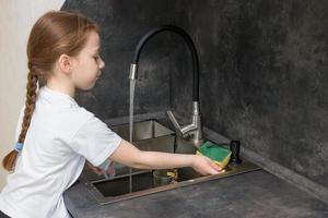 little girl with a pigtail washing dishes in the kitchen photo