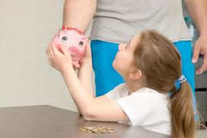 little daughter takes a piggy bank from her father's hands photo