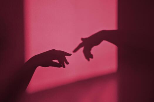 Metaphor of Adam by Michelangelo Creation through shadow on wall. Silhouette of gesture touch by humans hands. Image toned in color of the year 2023 viva magenta photo