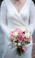 The bride in a white wedding dress is holding a bouquet of white flowers - peonies, roses. Wedding. Bride and groom. Delicate welcome bouquet. Beautiful decoration of weddings with leaves photo