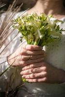 The bride in a white wedding dress is holding a bouquet of white flowers - peonies, roses. Wedding. Bride and groom. Delicate welcome bouquet. Beautiful decoration of weddings with leaves photo