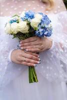 The bride in a white wedding dress is holding a bouquet of white flowers - peonies, roses. Wedding. Bride and groom. Delicate welcome bouquet. Beautiful decoration of weddings with leaves photo