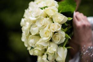 The bride in a white wedding dress is holding a bouquet of white flowers - peonies, roses. Wedding. Bride and groom. Delicate welcome bouquet. Beautiful decoration of weddings with leaves photo