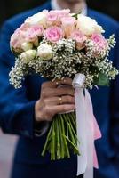 The bride in a white wedding dress is holding a bouquet of white flowers - peonies, roses. Wedding. Bride and groom. Delicate welcome bouquet. Beautiful decoration of weddings with leaves photo