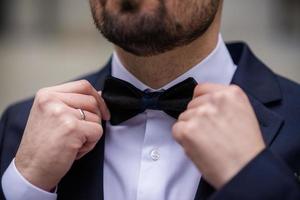 las manos de la pajarita del novio. padrinos de boda elegantes que ayudan al novio feliz a prepararse por la mañana para la ceremonia de la boda. hombre de lujo con traje en la habitación. día de la boda. foto