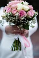 The bride in a white wedding dress is holding a bouquet of white flowers - peonies, roses. Wedding. Bride and groom. Delicate welcome bouquet. Beautiful decoration of weddings with leaves photo