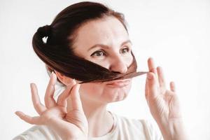 Portrait of a beautiful woman who makes a mustache out of pigtails and a funny face on a white background photo