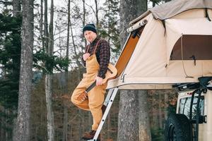 Adventurer man standing down on roof of the car with tent mounted on it for free travel camping lifestyle photo