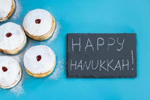 Happy Hanukkah. Jewish dessert sufganiyot donuts on blue background. Symbol of religious Judaism holiday. Inscription on chalk board. photo