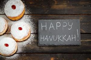 Happy Hanukkah. Traditional dessert Sufganiyot on dark wooden background. Donuts, candles and gifts. Celebrating Jewish holiday. photo