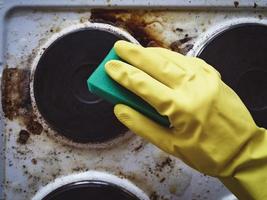 mano a mano lavando la estufa de la cocina desordenada foto