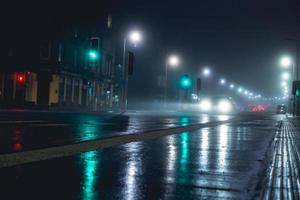 A lone car is seen driving through a misty night. The photo captures the ethereal atmosphere of the scene, with the glowing lights of the car and the surrounding city.