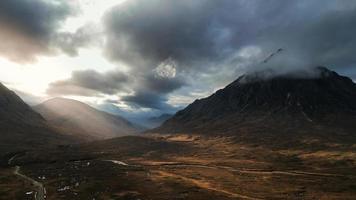 la impresionante belleza de glen coe, con los rayos dorados de dios brillando desde el cielo. la foto muestra el impresionante paisaje de las tierras altas escocesas, con colinas ondulantes y un río sinuoso.