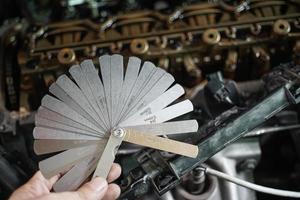 auto mechanic Using Feeler gauge Set the car valve. Measuring valve clearance with tappet feeler gauge set photo