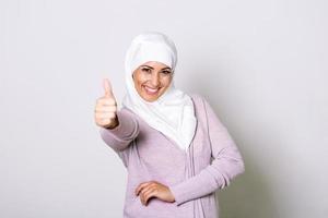 Smiling young middle eastern muslim woman looking at the camera with her thumbs up. Portrait of a beautiful muslim woman wearing hijab. Beautiful young Muslim woman wearing a hijab on her head photo