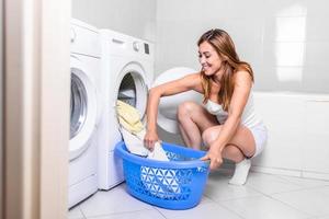 mujer cargando ropa en la lavadora, preparando el ciclo de lavado, cerca de una lavadora cargada de ropa, tomando a mano toallas de color foto