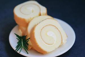 sponge cake roll slices sweets dessert cream roll vanilla snacks and food concept - Swiss Roll Cake, Cake roll on plate cake with rosemary on table photo