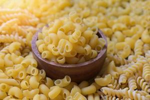 concepto culinario de comida italiana, pasta cruda para cocinar, macarrones crudos en tazón de madera, pasta varios tipos de espaguetis de pasta sin cocer y fideos en el fondo foto