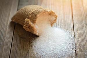 Sugar on sack and wooden background, white sugar for food and sweets dessert candy heap of sweet sugar crystalline granulated photo