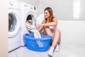 mujer joven sacando ropa de la lavadora en casa. mujer joven en casa, haciendo tareas domésticas y limpieza, recogiendo ropa y vestidos de la secadora de ropa, secadora foto