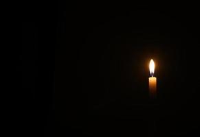 One yellow candle burns in black background photo