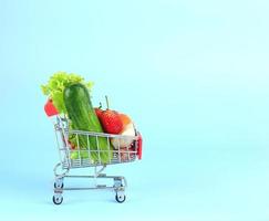 carrito de compras rojo lleno de varias verduras y frutas foto