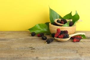 Close up of fresh mulberries and bowl of fruit against yellow background photo