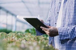 Futuristic businessman farms vegetables and crops using modern AI technology using mobile phones, temperature and humidity sensors, water tracking, climate control, holographic data data icons. photo