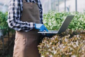 un hombre de negocios futurista cultiva verduras y cultivos usando tecnología moderna de inteligencia artificial usando teléfonos móviles, sensores de temperatura y humedad, rastreo de agua, control climático, íconos de datos holográficos. foto