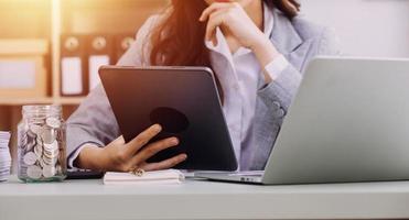 Young business woman sitting in office at table and using smartphone. On desk is laptop and tablet computer, on screen charts and graphs. Woman analyzing data. Student learning online. photo