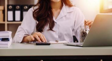 Young business woman sitting in office at table and using smartphone. On desk is laptop and tablet computer, on screen charts and graphs. Woman analyzing data. Student learning online. photo