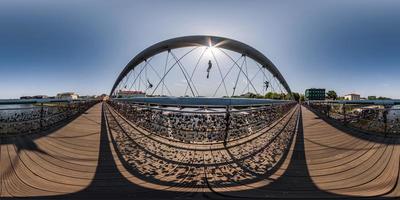 vista panorámica hdri 360 esférica completa sobre un puente colgante de madera para peatones con figuras monumentales de acróbatas sobre un río ancho en proyección equirectangular. para contenido vr ar foto