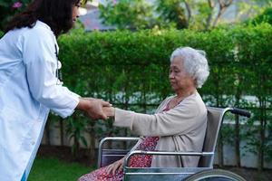 Doctor help Asian elderly woman disability patient sitting on wheelchair in park, medical concept. photo