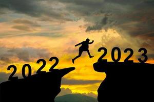 a businessman is jumping from a cliff in 2022 to a cliff in 2023 photo