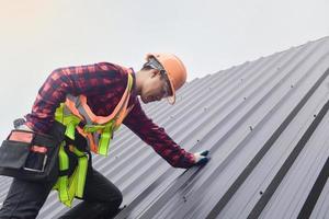 trabajador de techado con uniforme protector y guantes, herramientas para techos, instalación de techos nuevos en construcción, taladro eléctrico usado en techos nuevos con láminas de metal. foto