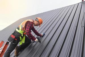 trabajador de techado con uniforme protector y guantes, herramientas para techos, instalación de techos nuevos en construcción, taladro eléctrico usado en techos nuevos con láminas de metal. foto