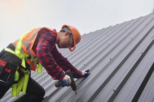 trabajador de techado con uniforme protector y guantes, herramientas para techos, instalación de techos nuevos en construcción, taladro eléctrico usado en techos nuevos con láminas de metal. foto