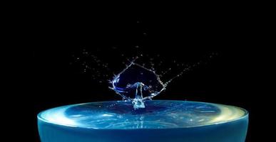 A splash of blue water with a drop flying from above on a black background photo