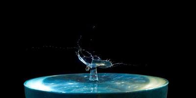 un chorro de agua azul con una gota volando desde arriba sobre un fondo negro foto