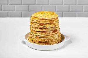 Stack of freshly baked pancakes lie in white ceramic form. photo