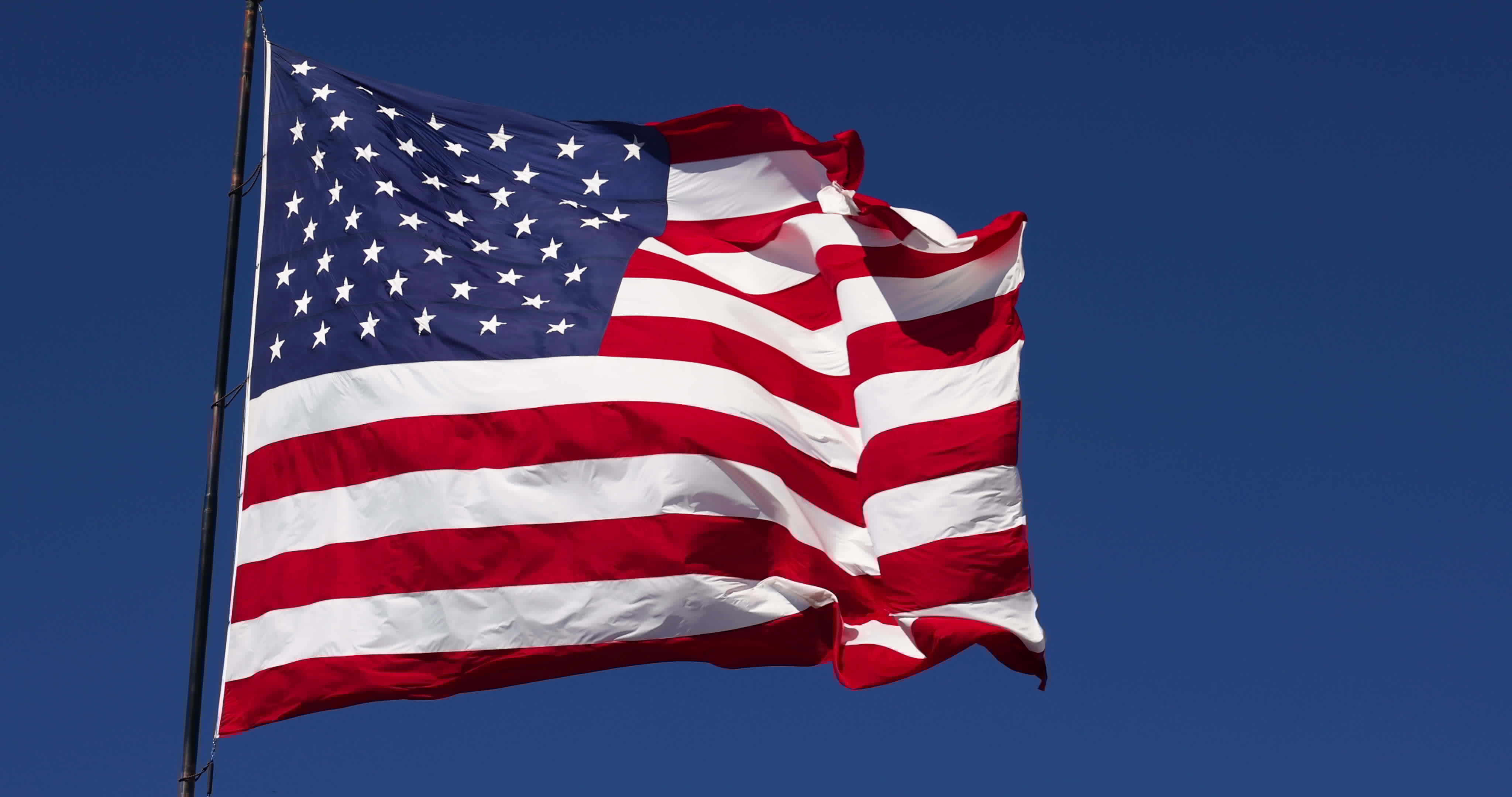 Slow Motion Real American Flag Waving In Wind Against a Deep Blue Sky