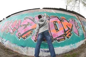 A young guy in a gray hoodie paints graffiti in pink and green c photo