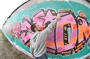 A young guy in a gray hoodie paints graffiti in pink and green c photo