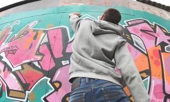 A young guy in a gray hoodie paints graffiti in pink and green c photo